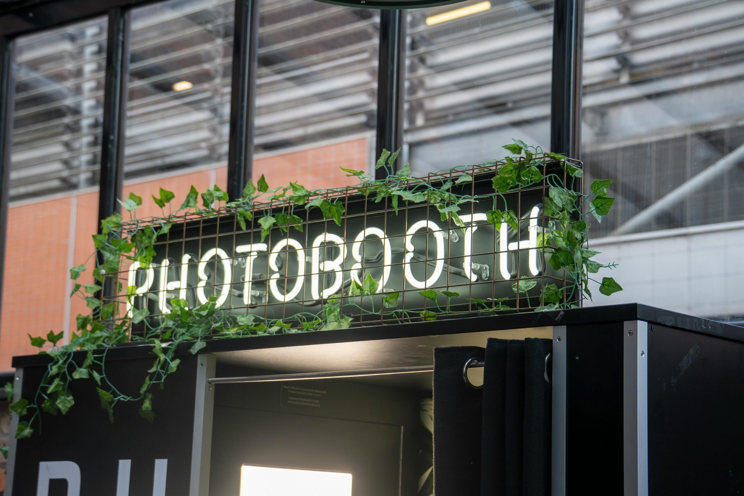 Un photomaton moderne avec une enseigne lumineuse au néon et des plantes, idéal pour un événement contemporain à Paris.
