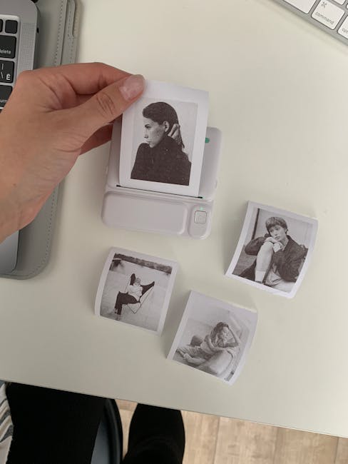 A hand using an instant photo printer to create black and white portraits on a desk.