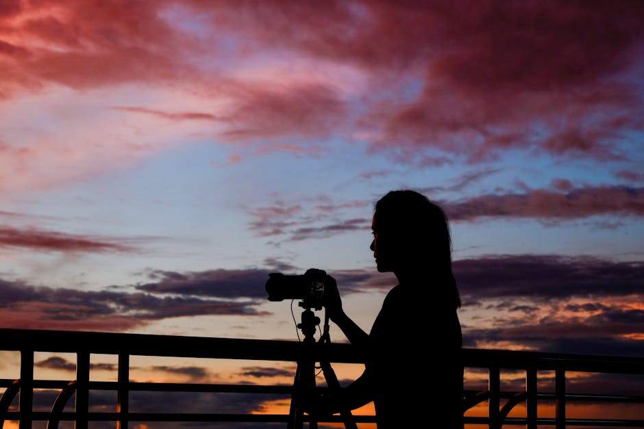 Silhouette of a woman with camera and tripod capturing a stunning sunset sky.